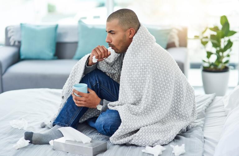 Young Hispanic man sick in bed with cough due to cold, flu or bronchitis