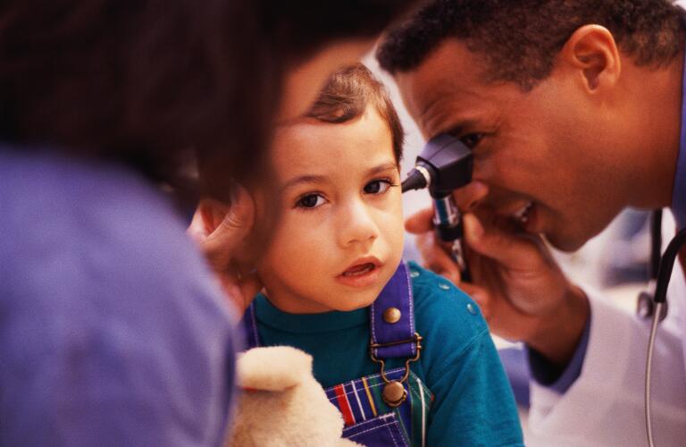 Doctor checking boy's ear; mother in foreground