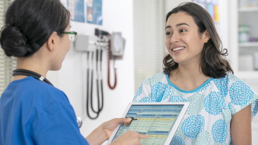 Young Hispanic woman in medical gown smiling nurse or technician holding digital tablet