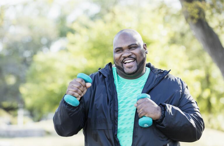 Older overweight African American man outdoors smiling and walking with hand weights