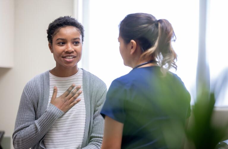 African American female patient with hand on chest talking to nurse during doctor's appointment