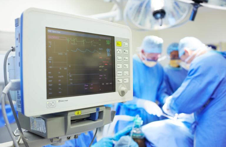 Close-up of heart monitor with surgeons in background in operating room