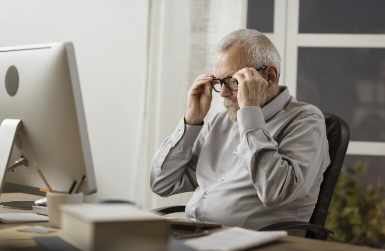 Senior man at computer adjusting eyeglasses