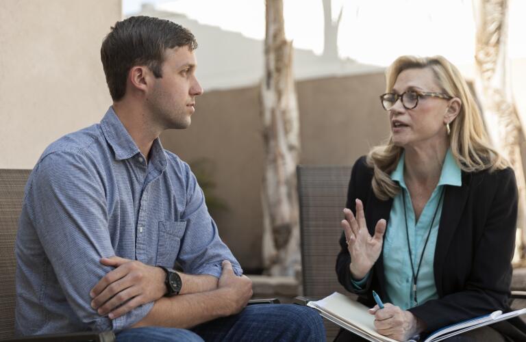 Young Caucasian man talking to middle aged female Caucasian therapist in outdoor setting