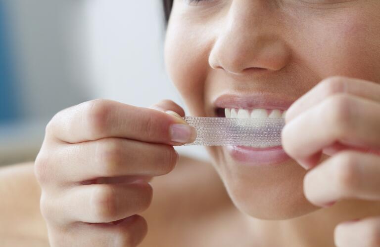 Close up of young woman using a teeth whitening strip