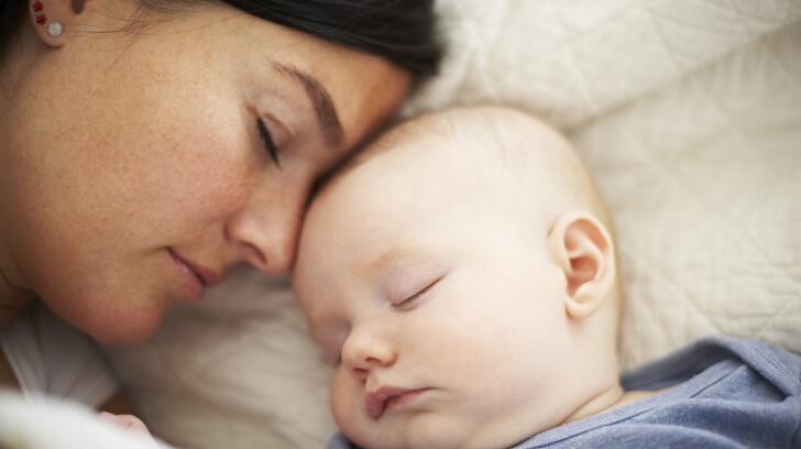 Young Caucasian mother sleeping next to newborn baby