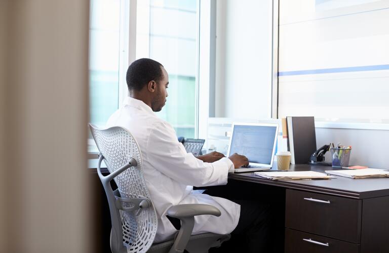 African American male doctor typing on laptop at desk in office