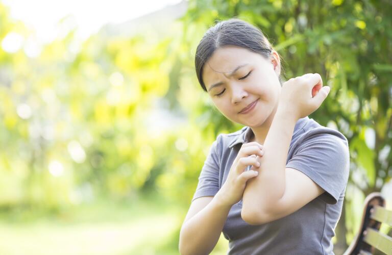 woman outside scratching arm