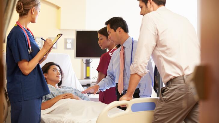 Medical Team Meeting Around Female Patient In Hospital Room