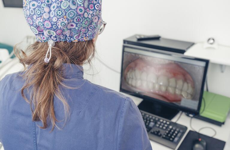 Rear view of female dentist looking at images of patient's bite on computer monitor in dental clinic