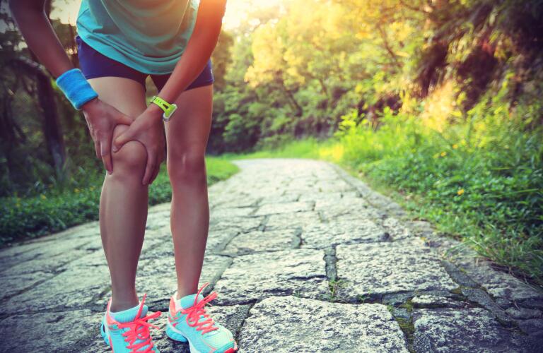 Cropped image of female Caucasian runner holding knee in pain on outdoor path