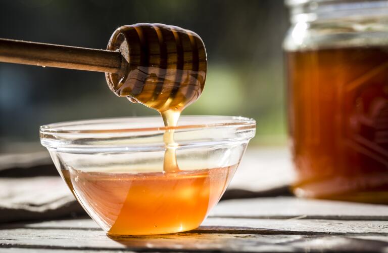 honey dripping off honey spoon into bowl