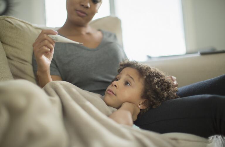 Mother measuring temperature of daughter on sofa