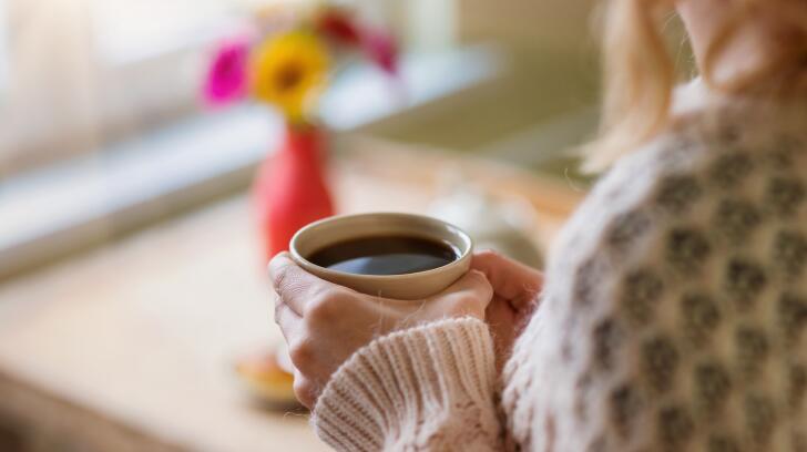 unidentifying woman holding cup of coffee with flowers in background