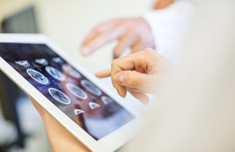 Unseen Caucasian doctors looking at brain scan images on tablet
