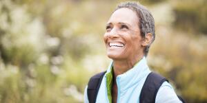 smiling senior woman with backpack hiking outdoors
