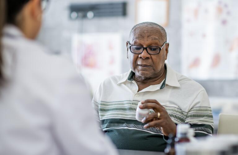 Senior African American male patient holding prescription bottle with doctor