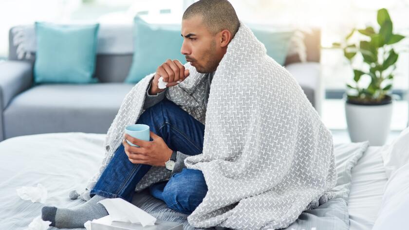 Young Hispanic man sick in bed with cough due to cold, flu or bronchitis
