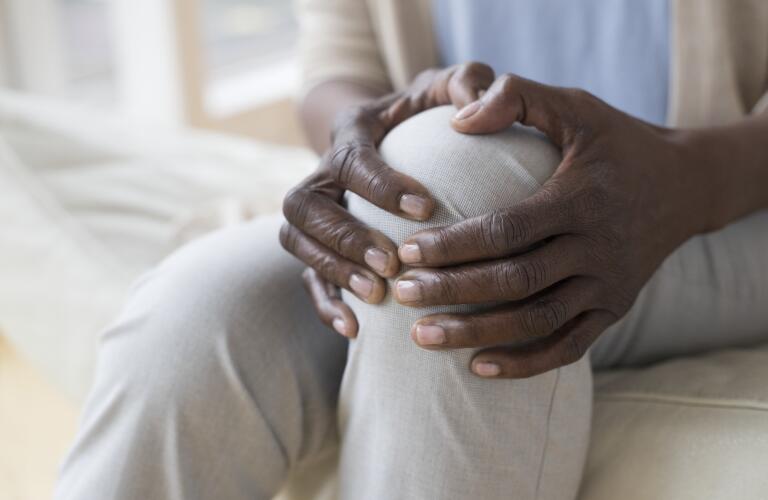 Close-up of unseen African American woman's hands holding knee in pain