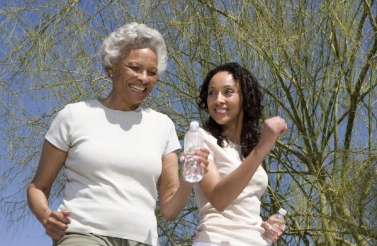 African american mother and daughter jogging together against blue sky