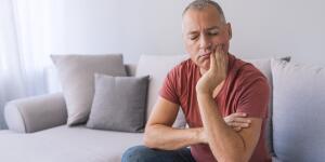 Caucasian man on couch holding mouth in pain or discomfort