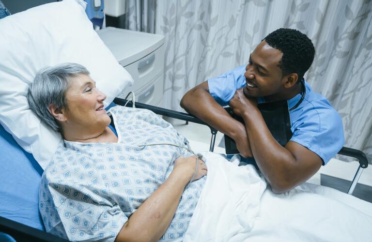Young male African American doctor or nurse talking to older female Caucasian patient in hospital bed