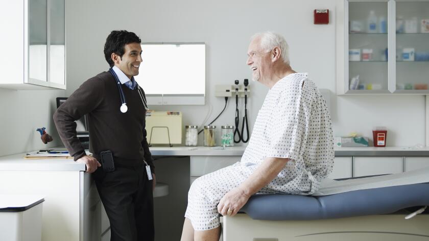 Senior male patient in hospital gown talking to male doctor
