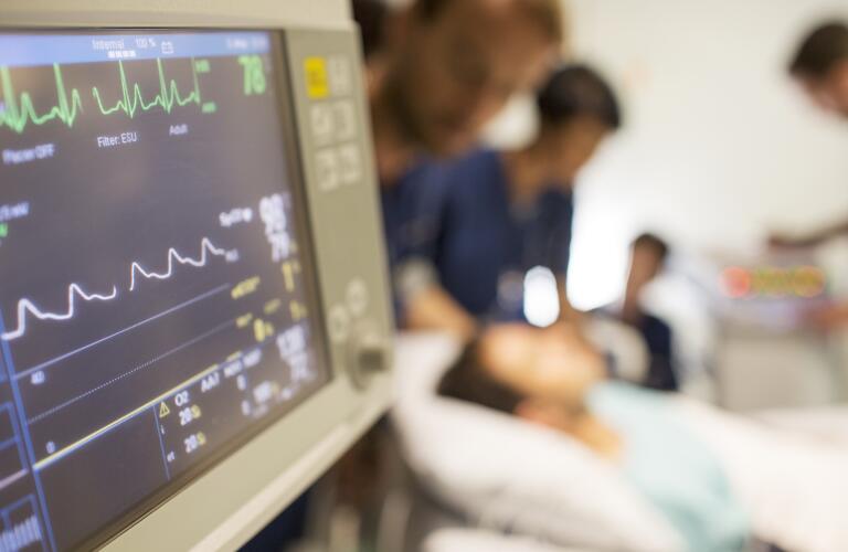 Heart rate monitor, patient and doctors in background in intensive care unit