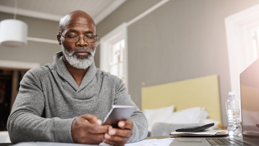 senior African American man holding smartphone in front of laptop