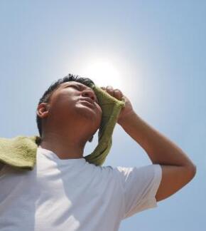 Young Asian American man wiping sweat off forehead with towel under direct sunshine