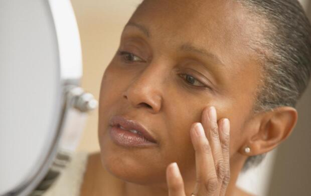 middle age African American woman looking at skin in mirror middle age African American woman looking at skin in mirror