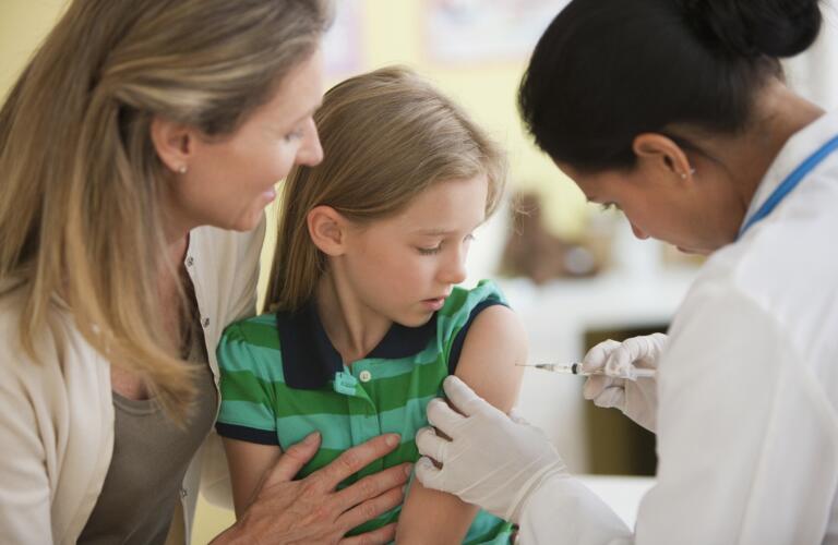 Doctor giving girl injection while mother watches