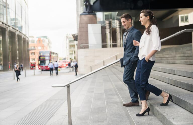 Rear view of young businessman and woman chatting whilst walking down stairway, London, UK