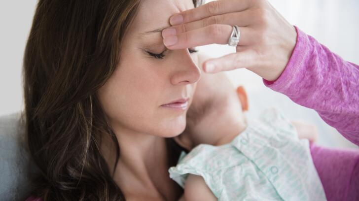 Caucasian mother with infant holding her head with headache, fatigue or postpartum depression