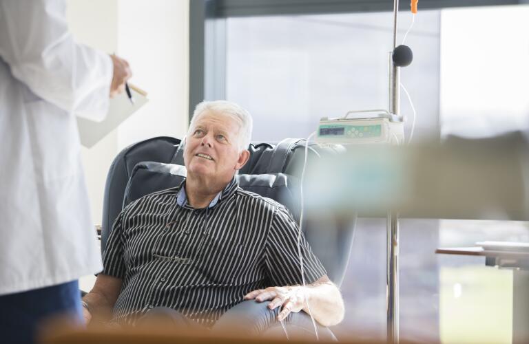 senior Caucasian male receiving chemotherapy in hospital speaking with doctor