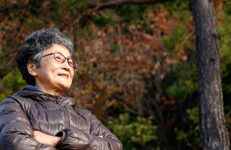 confident senior woman in forest wearing jacket while hiking