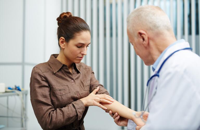 Older Caucasian male doctor examining arm of young female patient for moles, rash or skin tag