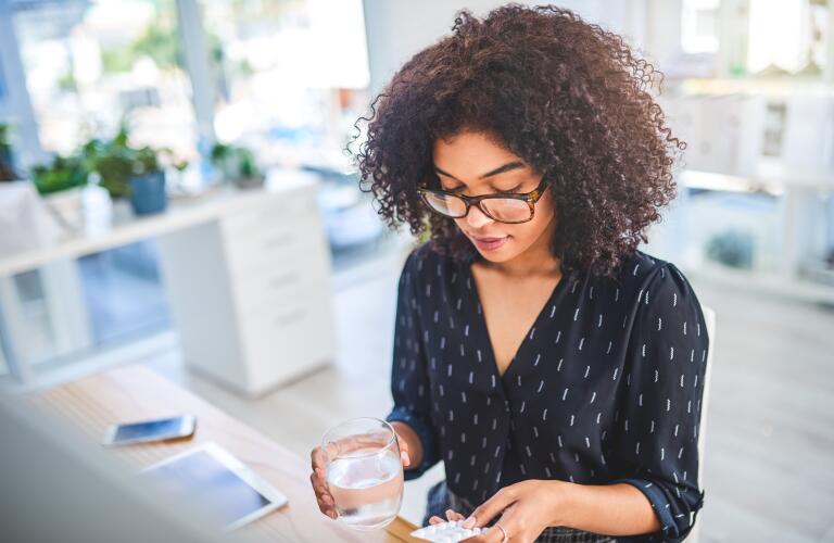 young African American woman holding glass of water and pills