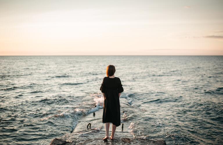 Young woman standing on rock looking at ocean