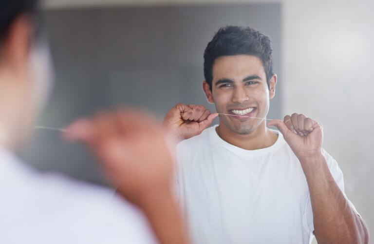 smiling man flossing teeth in mirror