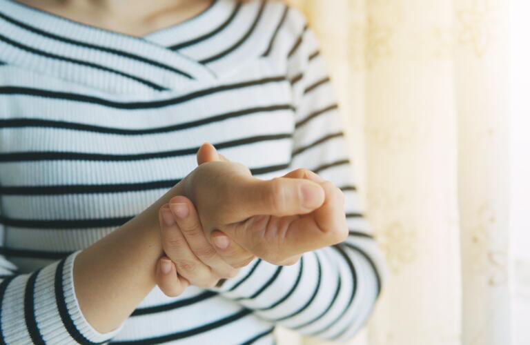 woman holding her hand and wrist with fingers curled into fist
