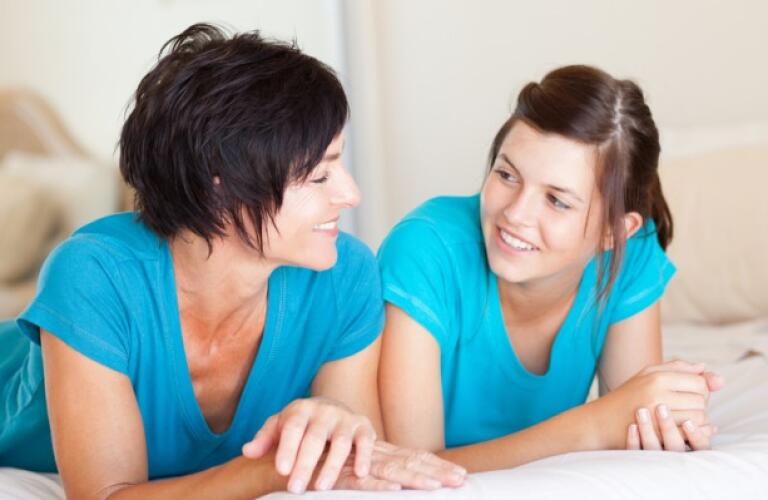 Middle aged mother and teen daughter chatting on bed