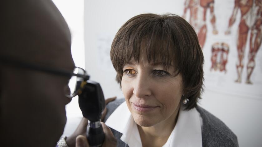 male African American eye doctor examining eyes of middle aged female Caucasian female