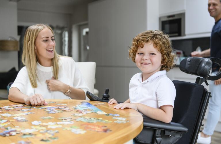 Caucasian boy with muscular dystrophy or other neuromuscular disease in wheelchair with family in kitchen smiling