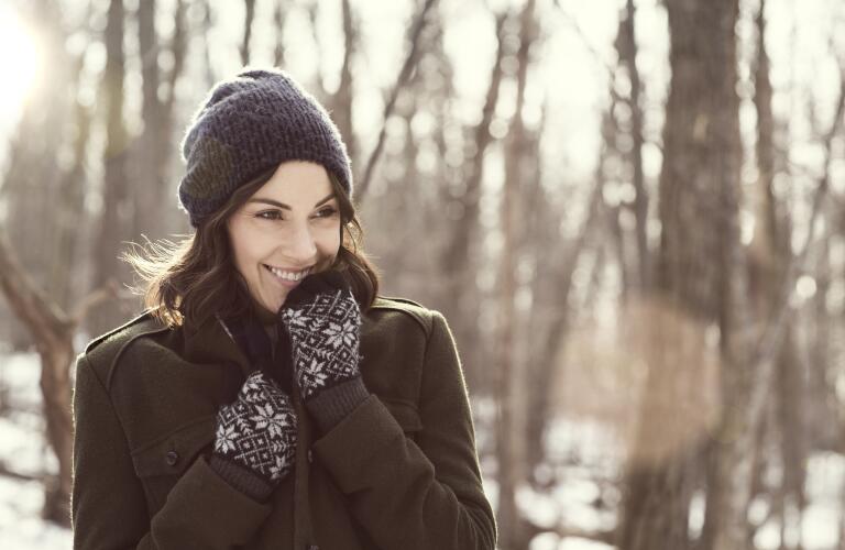smiling young Caucasian brunette woman wearing beanie hat and gloves during the winter backlit by sunshine