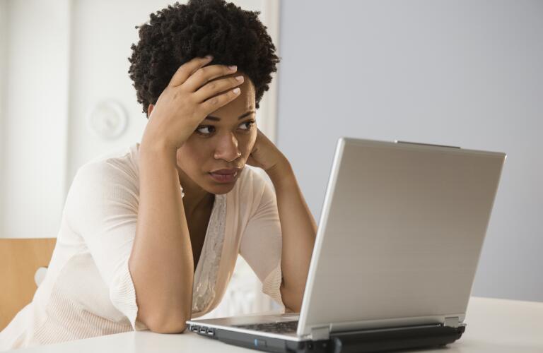 frustrated African American woman with hand on forehead looking at laptop