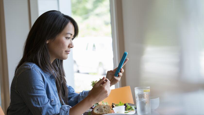 woman eating salad and checking phone