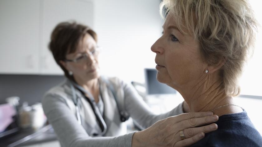 female doctor examining female patient's neck and shoulder