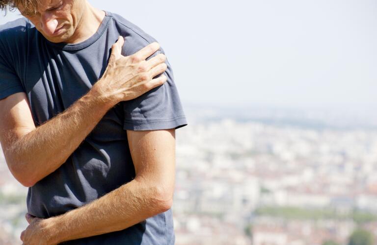 Man outdoors holding shoulder in pain