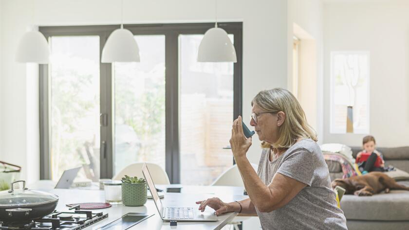 woman sitting at kitchen table in front of laptop using inhaler